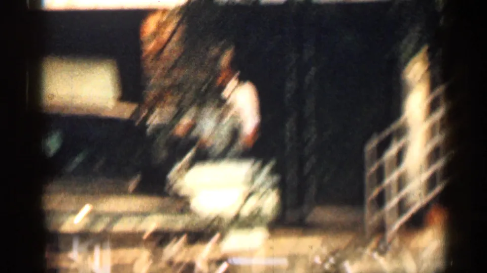 Soft 1963 Texas 8mm frame showing a person in a light shirt near an olive-green car on a brick-lined residential block.