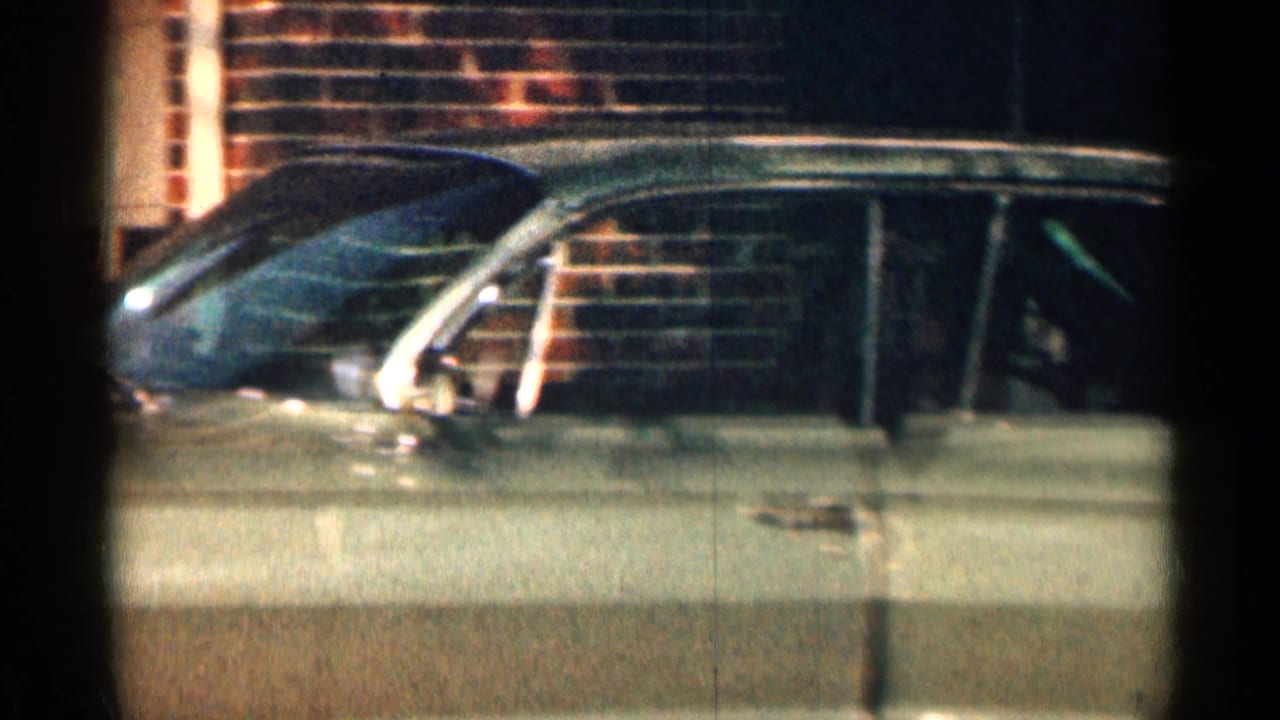 Light-colored classic sedan parked beside a brick wall with a side door ajar.