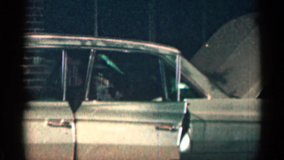 Side view of a 1963 Texas home-movie sedan with the hood raised and one door ajar against a dark exterior.
