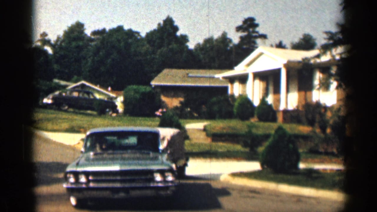 1963 Texas home-movie frame of a large sedan driving toward the camera on a quiet residential street.