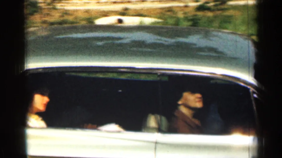 1963 Texas home-movie frame with a woman passenger and driver visible inside a classic sedan in motion.