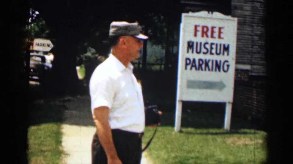1963 Texas 8mm frame showing a man beside a brick building and a sign reading FREE MUSEUM PARKING.