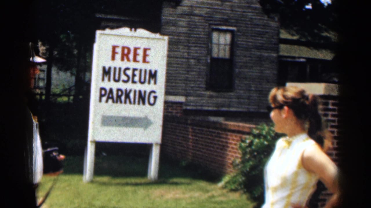 1963 Texas home-movie frame showing a Free Museum Parking sign near a building, with a woman partly visible at right.