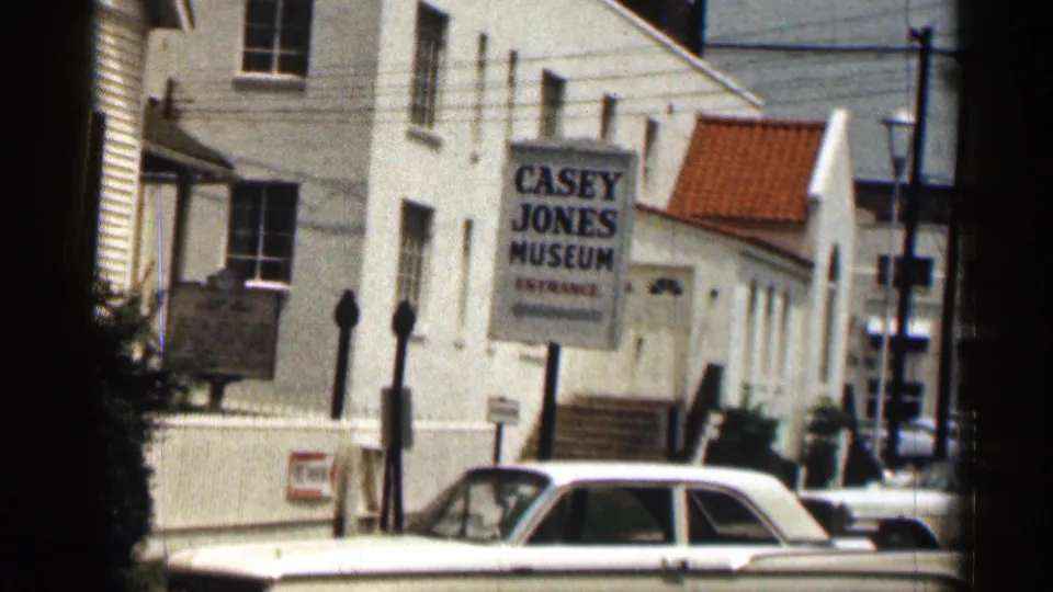 1963 Texas home-movie view of the Casey Jones Museum sign on a white building, with a white sedan at the curb.