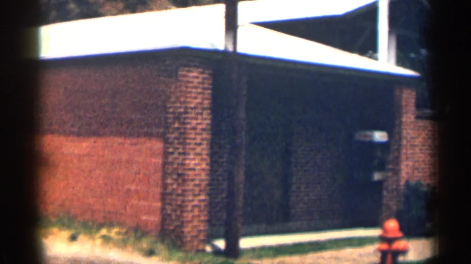 1963 Texas exterior showing a dark doorway or entrance, brick wall, sign-like detail, sidewalk, and red fire hydrant.