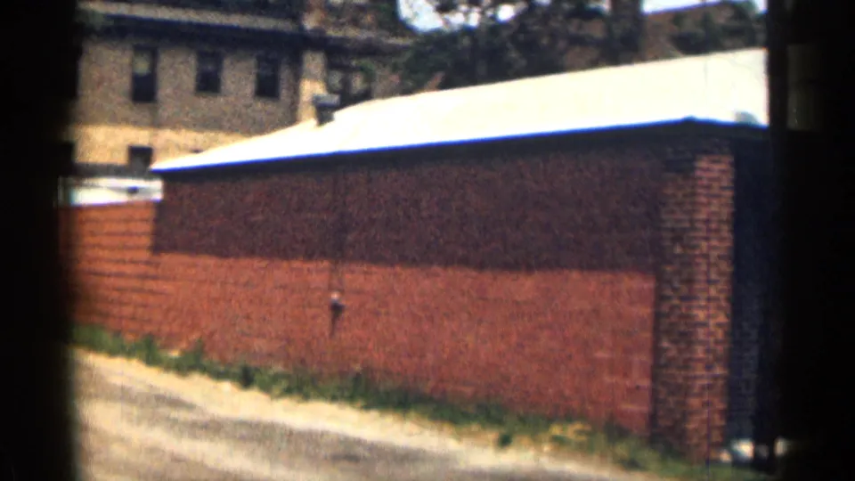 A 1963 Texas street-side brick wall with pale roofline, curb, grass strip, and background buildings.