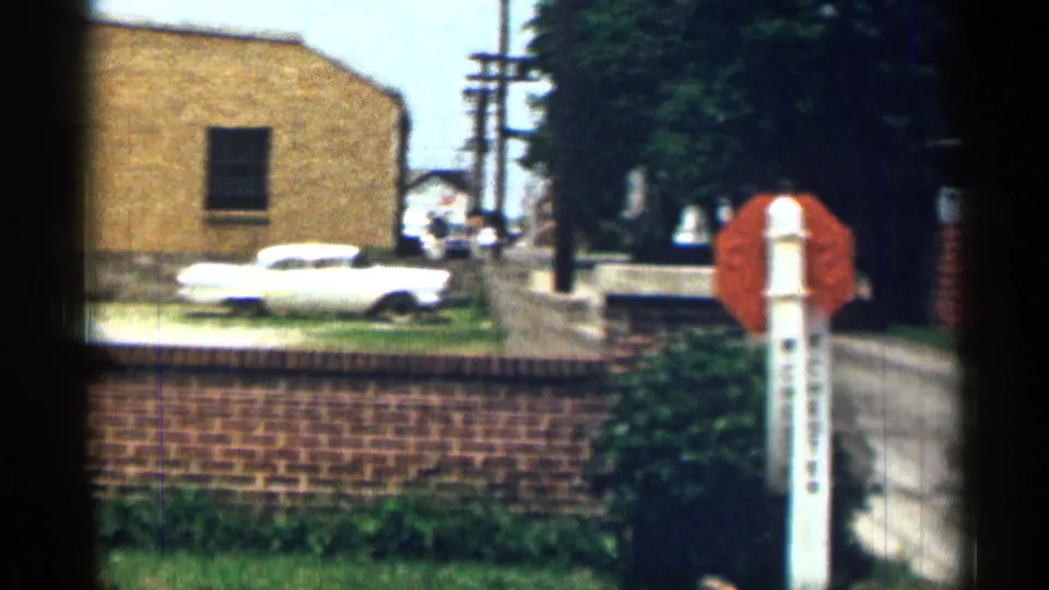 1963 Texas frame showing the W CHESTER stop sign area with a brick wall, dirt road, utility poles, and a white 1960s car.
