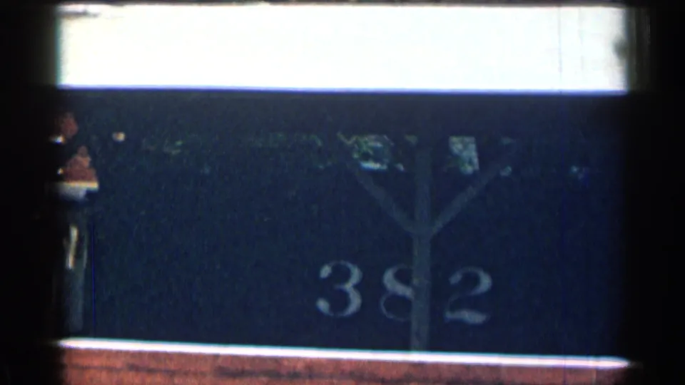 Close 8mm frame of a dark numbered surface marked 382, with a brick or reddish ledge along the lower edge.