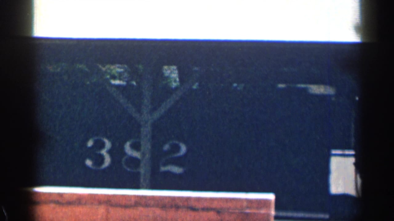 1963 Texas home-movie frame showing a dark stationary train car with the number 382, partly blocked by a foreground post or window edge.