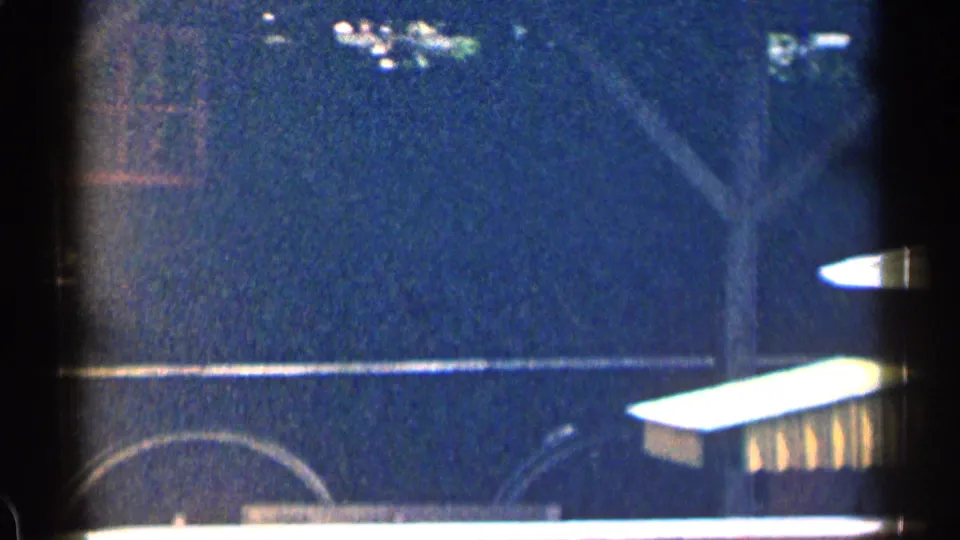 A close fixed view of the stationary rail car shows the dark car side, partial wheel outline, and bright foreground shapes in 1963 Texas footage.