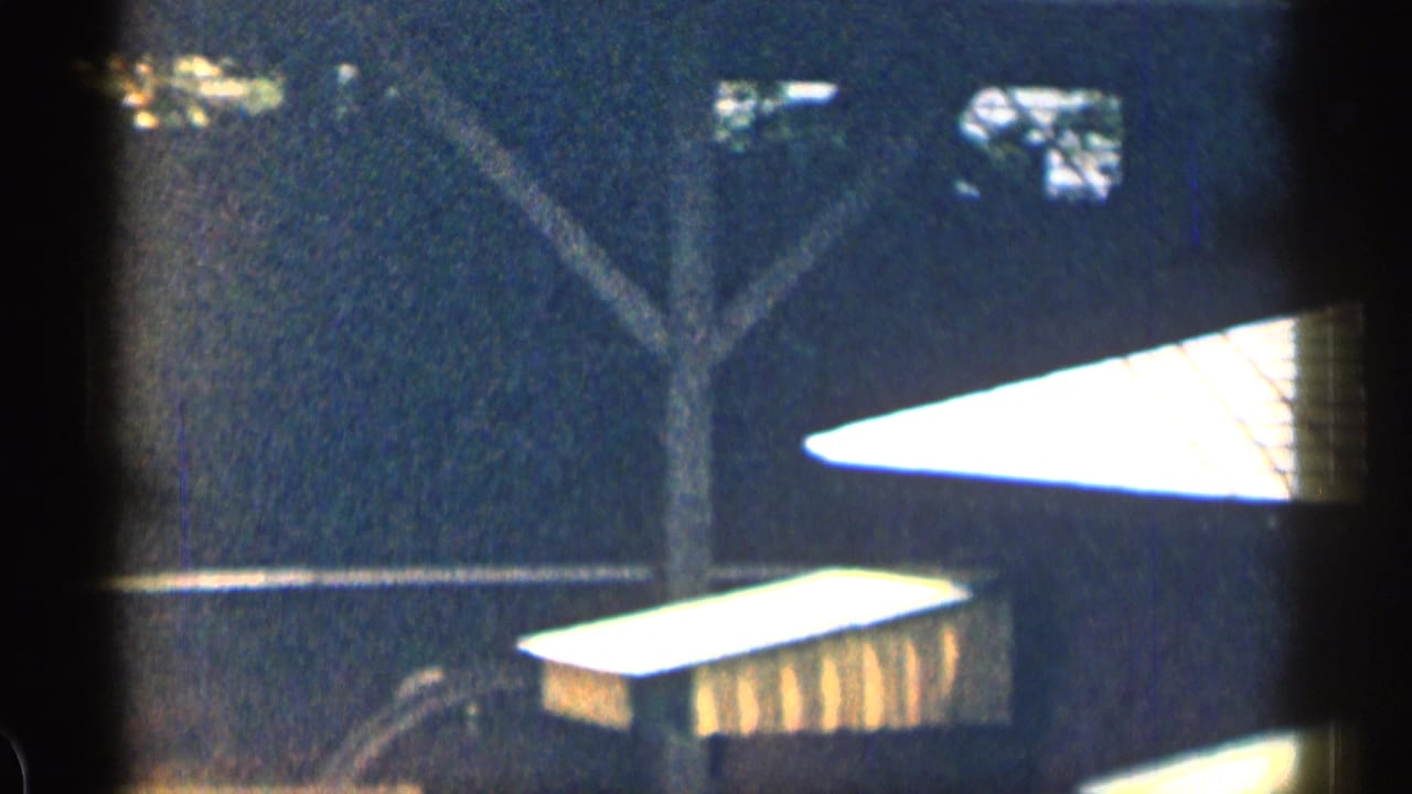 Dark, grainy view of a house exterior with shaded rooflines and nearby structural details.