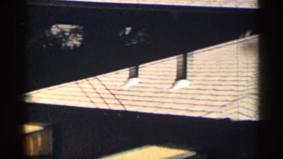 1963 Texas home-movie frame of a sloped shingle roof and chimney, partly obscured by dark film edges.