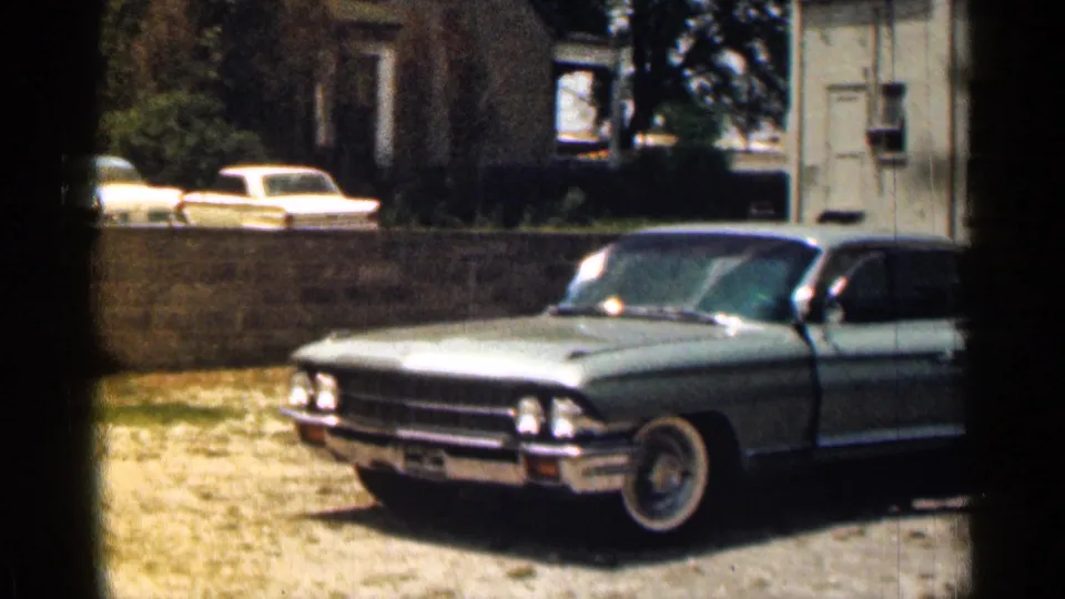 1963 Texas 8mm frame showing a blue mid-century sedan parked by a low wall in a sunny residential driveway.