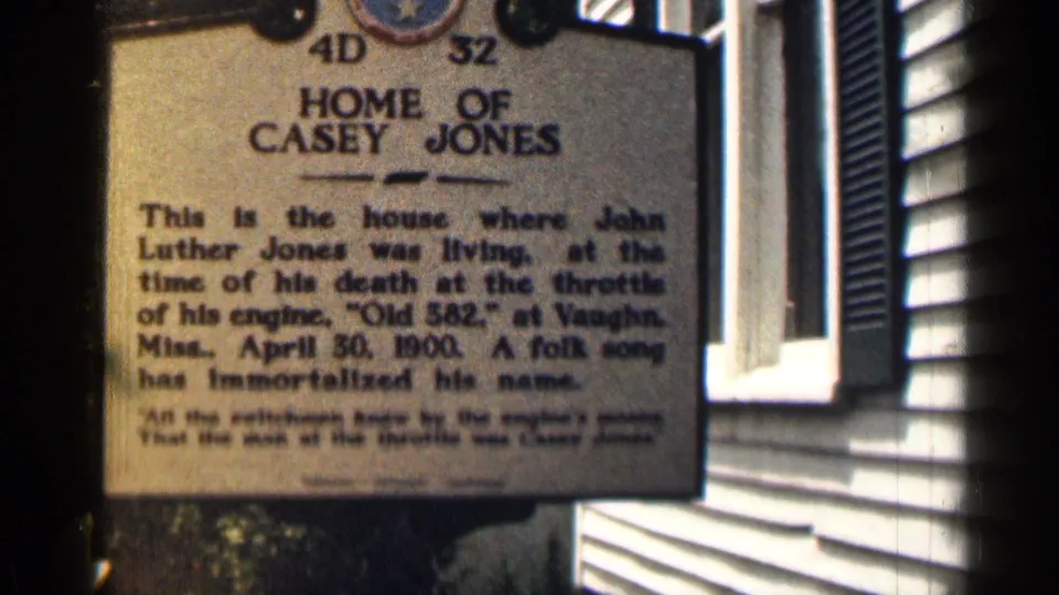 Close 8mm view of the Casey Jones marker, with readable commemorative text and building siding behind it.