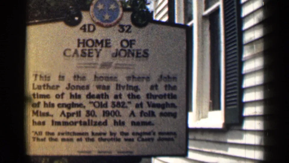 1963 Texas home-movie frame with a softer handheld view of the Home of Casey Jones marker and adjacent window trim.