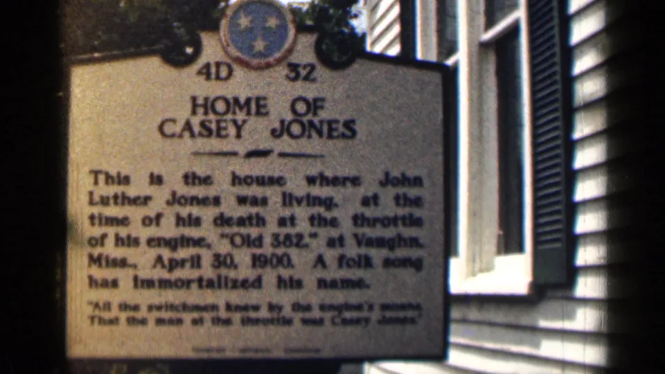 1963 Texas 8mm frame showing the Home of Casey Jones marker, commemorative text and sunlit exterior siding near a shuttered window.