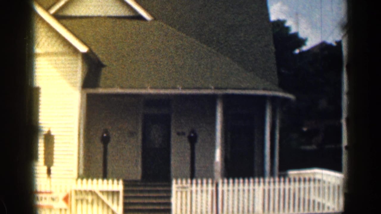 1963 Texas 8mm frame showing a white clapboard house with shaded porch, front steps, and a picket fence.
