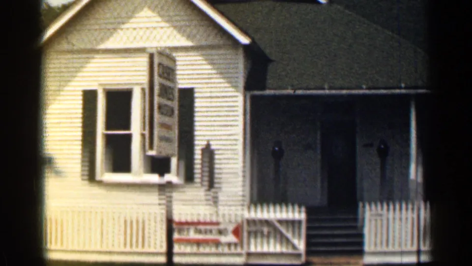 1963 Texas 8mm view of a white clapboard house facade with a window, roadside sign, porch, and picket fence.