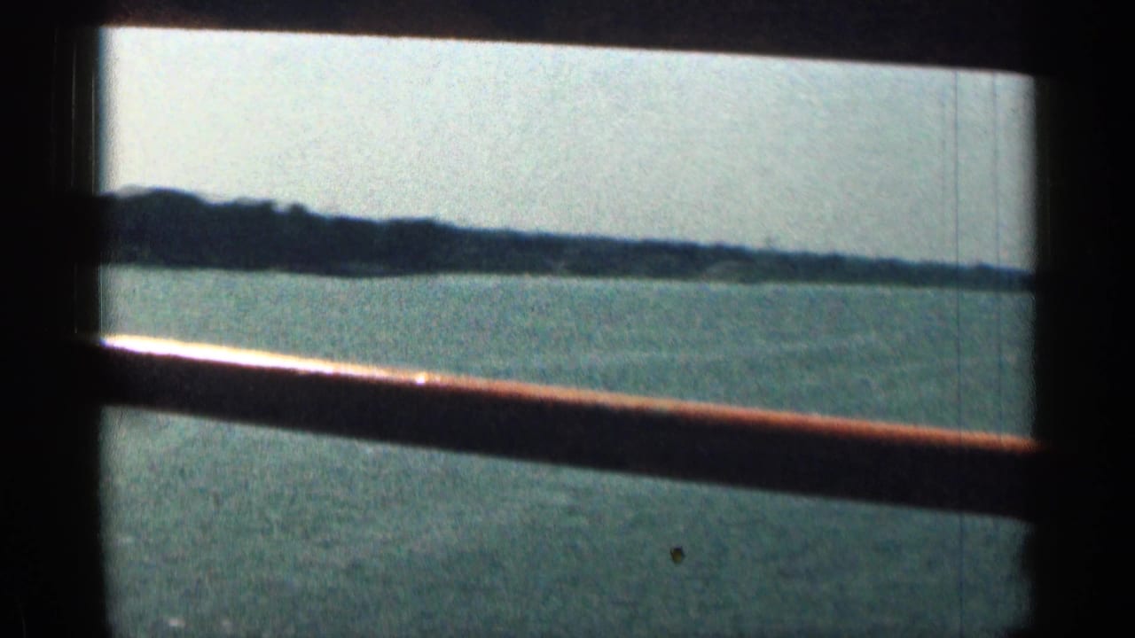 Wide river seen past bridge railing, with a low shoreline in the distance.