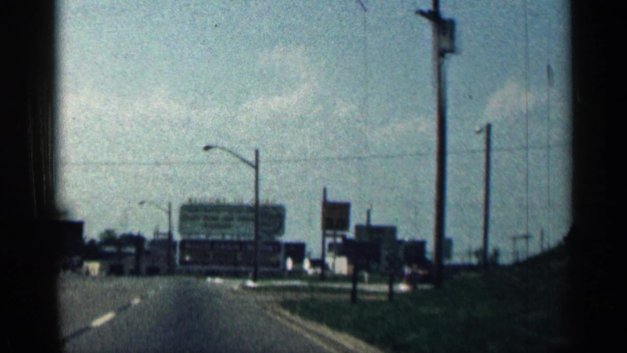 1963 Texas home-movie view from a moving vehicle approaching roadside signage, streetlights, and low commercial buildings.