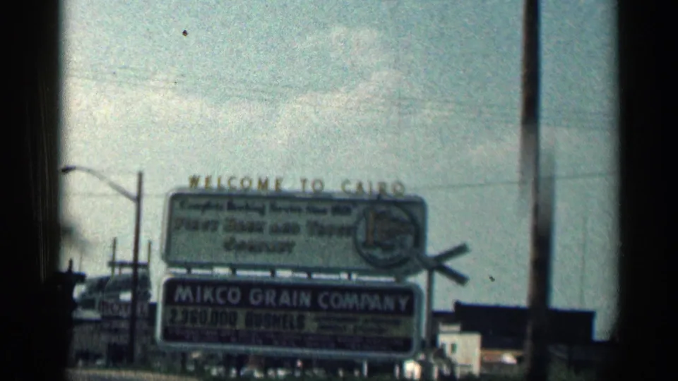 1963 Texas frame showing a Welcome to Cairo sign and Mikco Grain Company billboard beside the road, with utility poles and sky behind.