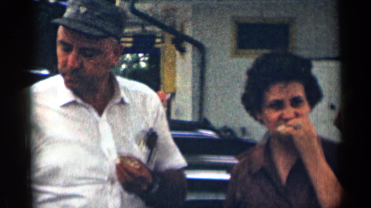Older man in a cap holds food while a woman eats beside him outdoors.