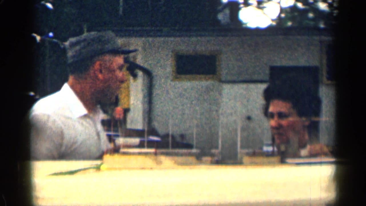 Man in a cap speaks with a woman near a motor lodge interior or entrance area.