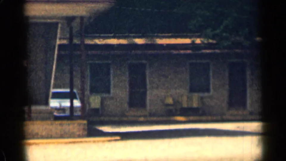 A white car is parked outside the Texas motor lodge, with doors, windows, and shaded facade details visible.