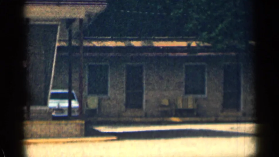 1963 Texas 8mm frame showing a low motor lodge exterior with shaded windows, outdoor chairs, trees, and a parked white car.