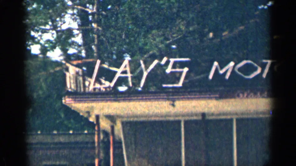 1963 Texas 8mm frame showing part of the Lay's Motor Lodge sign above the motel facade, with trees and balcony railing in view.