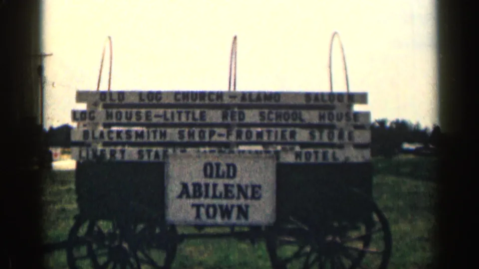 1963 Texas home-movie frame showing an Old Abilene Town sign with listed frontier-style attractions and wagon wheels below.