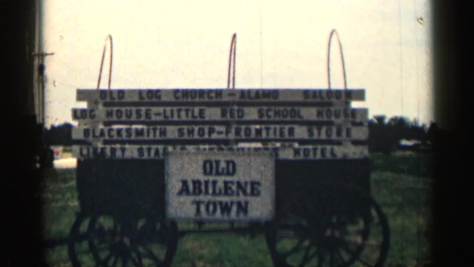 1963 Texas frame showing the Old Abilene Town attraction sign with frontier listings, wagon wheels, and soft 8mm exposure.