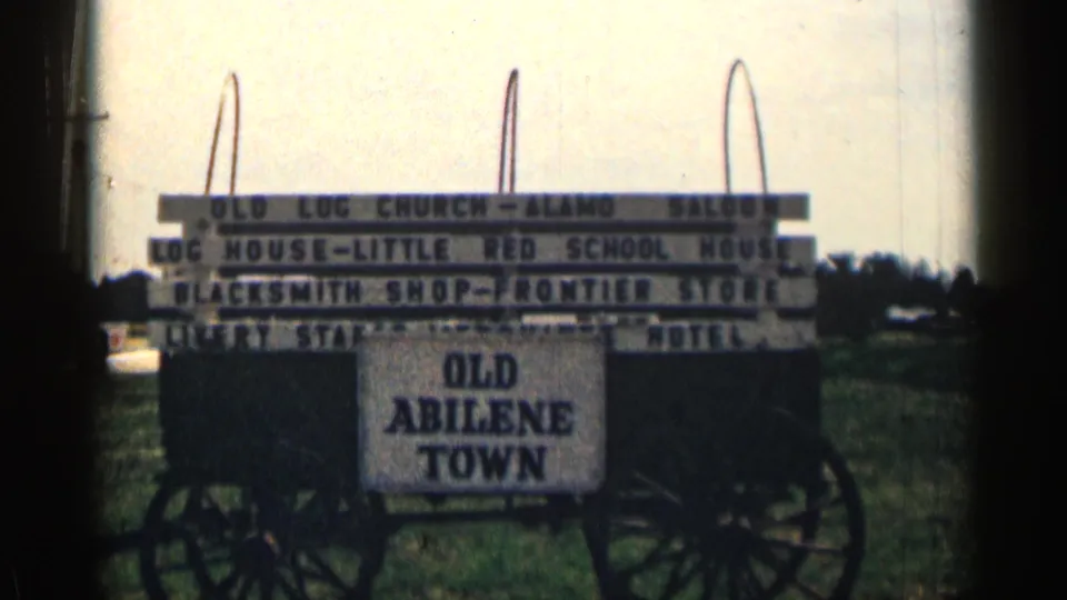 1963 Texas 8mm frame of a wagon-mounted Old Abilene Town sign with attraction names visible in bright outdoor light.