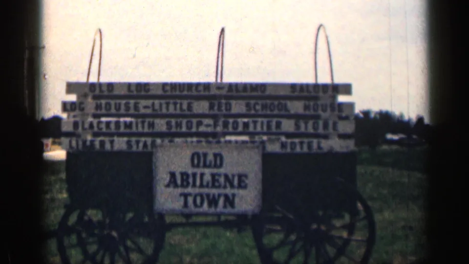 1963 Texas home-movie frame showing the Old Abilene Town wagon sign with attraction boards and soft 8mm exposure.