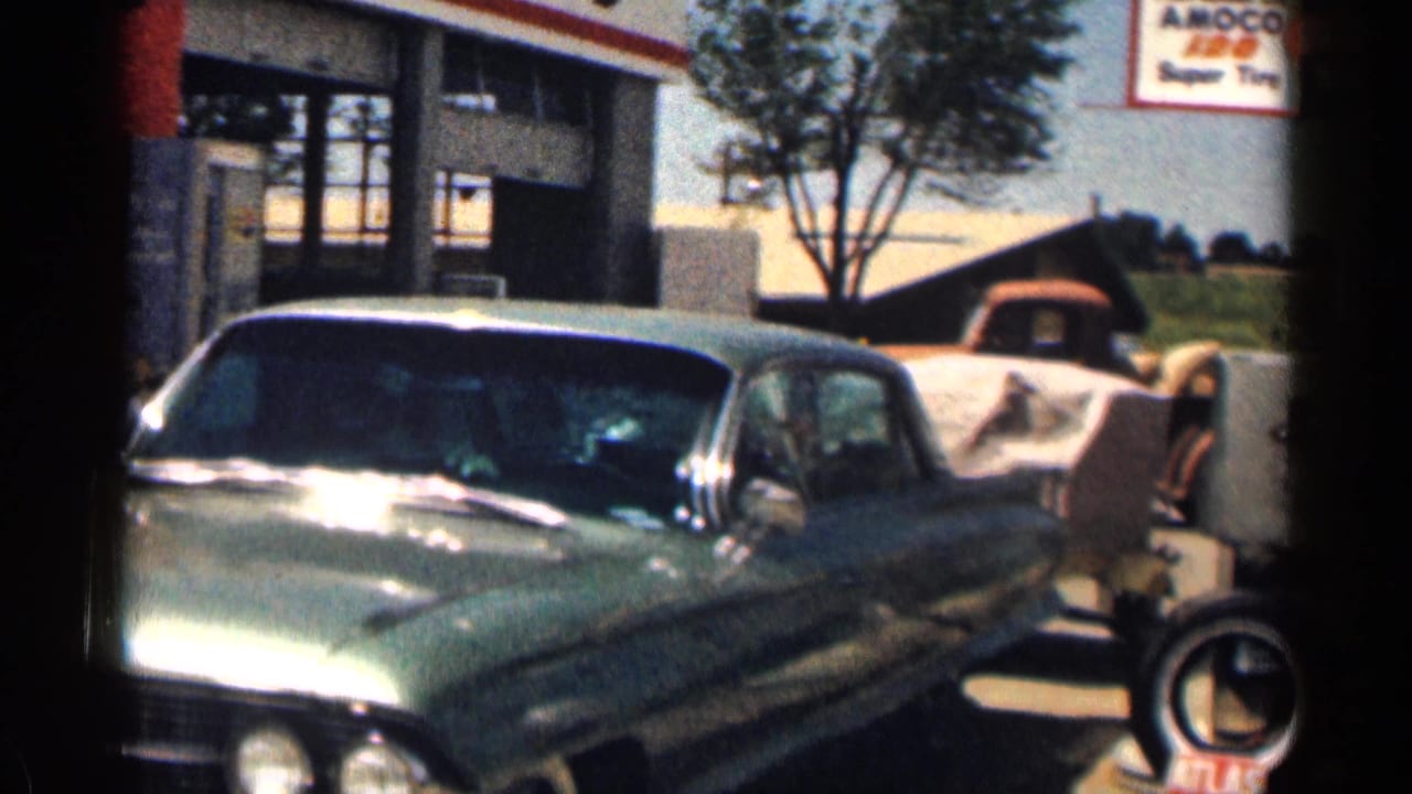 1963 Texas 8mm frame showing a green sedan at a sunny gas-station forecourt with Amoco and tire signs visible.