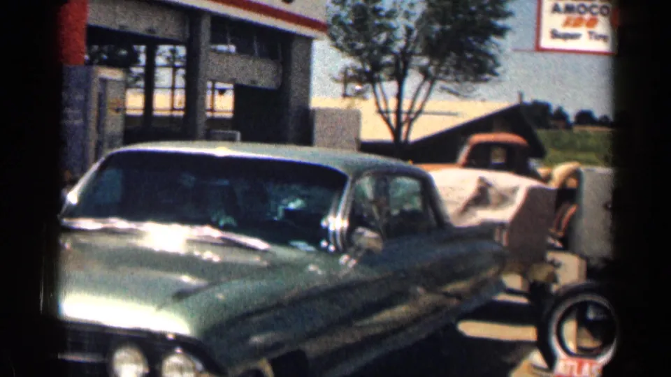 1963 Texas 8mm frame showing a green sedan at a sunny gas-station forecourt with Amoco and tire signs visible.