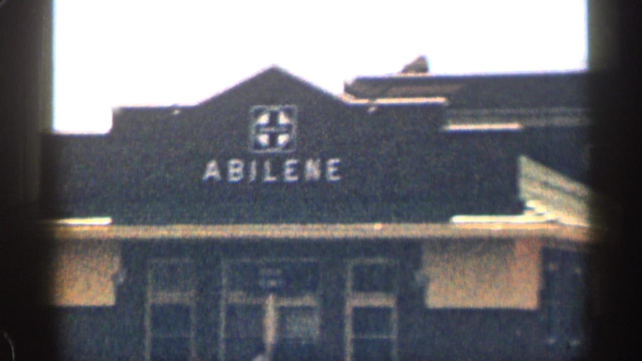 Dark building facade with ABILENE lettering, seen through film gate edges.