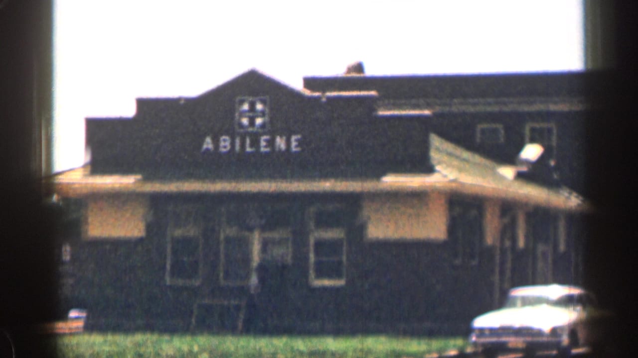 Abilene building exterior with grass verge and a white car at the right edge.