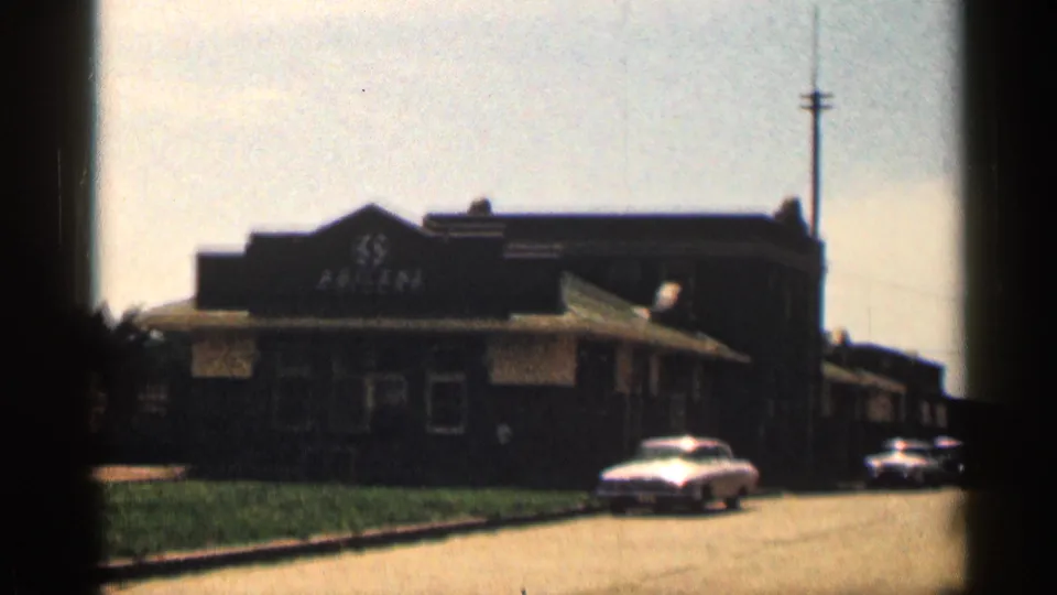 Late frame of the 1963 Texas street scene with the Abilene building, roadway, parked cars, and film edge shadow.