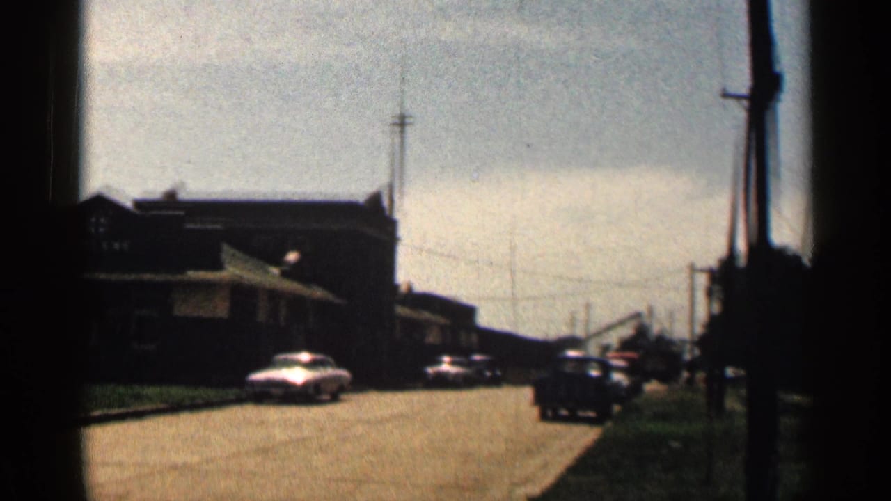 Roadside building and several classic cars along a sunlit street.