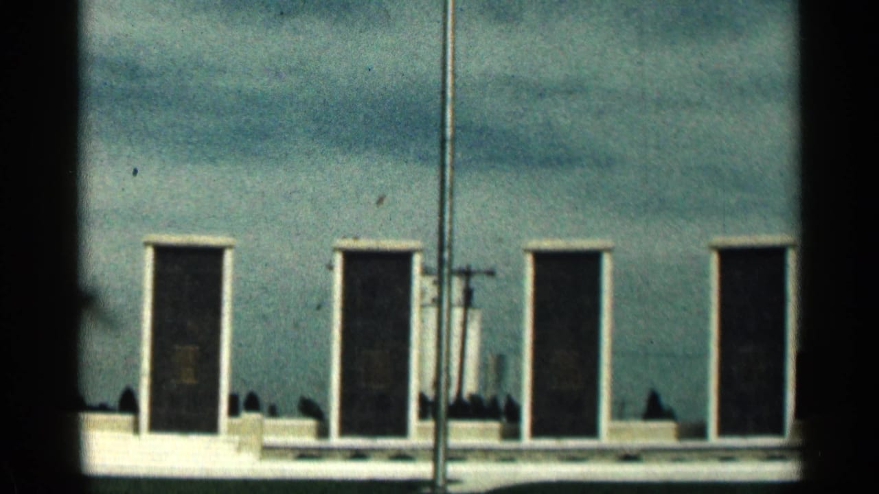 Flagpole in front of a low memorial wall with dark rectangular plaques under a cloudy sky.