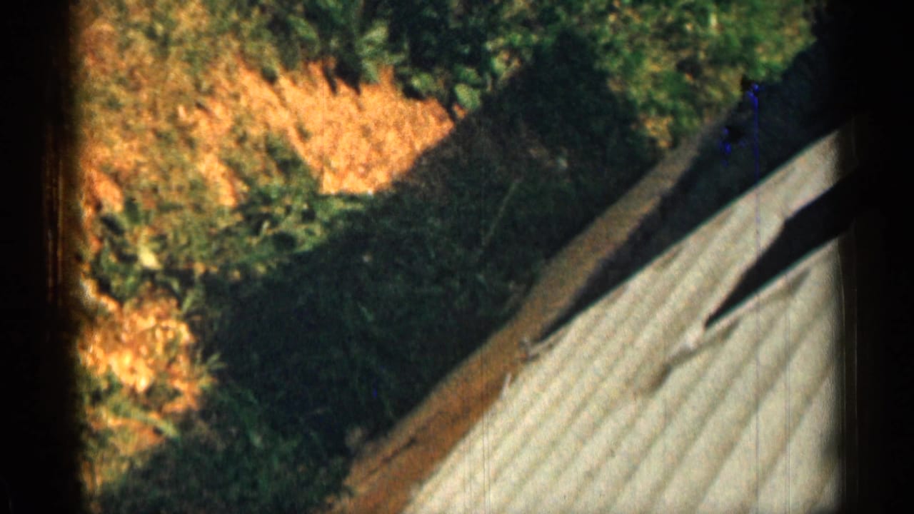 A 1963 Texas home-movie frame shows a brief tilted view of an outdoor walkway or roofline near grass and foliage.