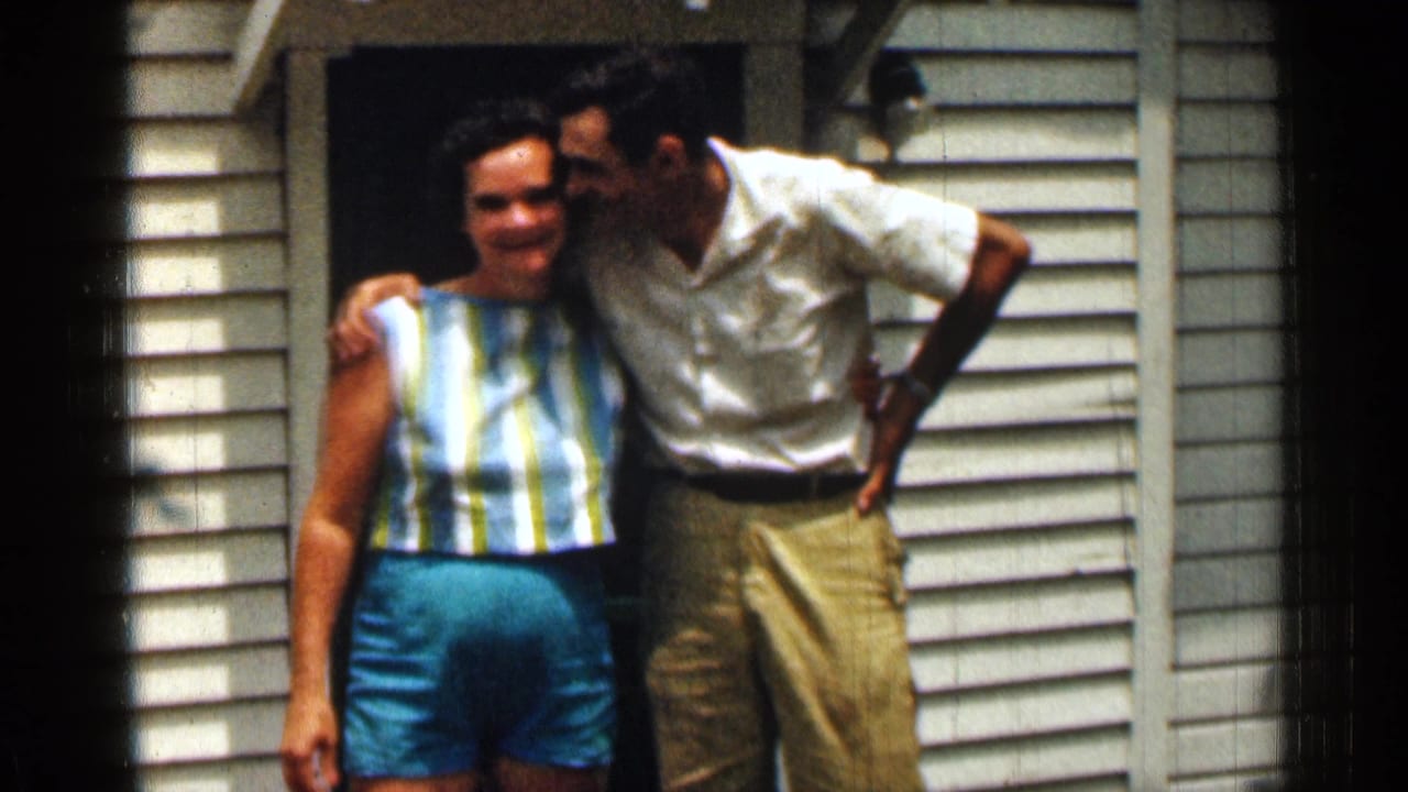 A smiling couple stands arm in arm outside a house doorway.