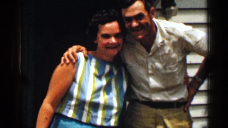 A closer 1963 Texas home-movie frame shows the couple smiling with arms around each other beside the house doorway.
