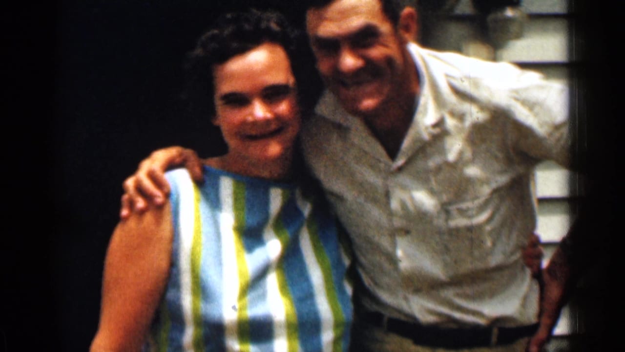 In 1963 Texas home-movie footage, an adult couple smiles outside a residence, with the man placing an arm around the woman.