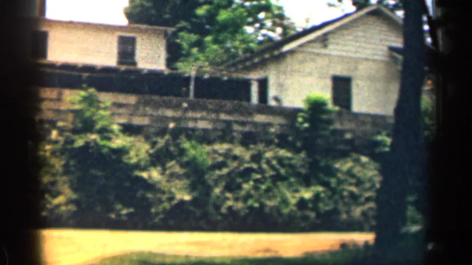 A 1963 Texas residential view shows house exteriors, a stone wall, trees, and a sunlit yard in handheld 8mm framing.