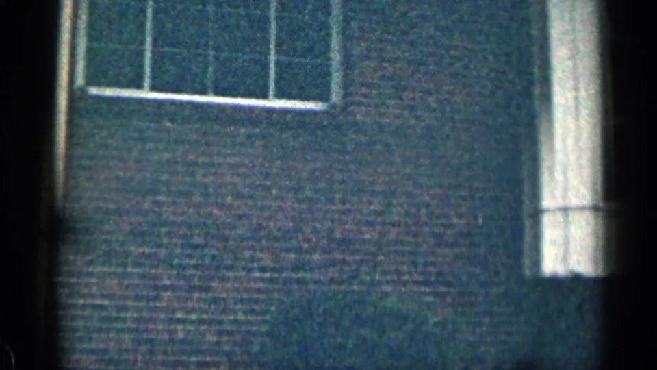 1963 Texas 8mm frame with a close pass across a brick facade, tall white trim, partial windows, and a dark vertical film edge.
