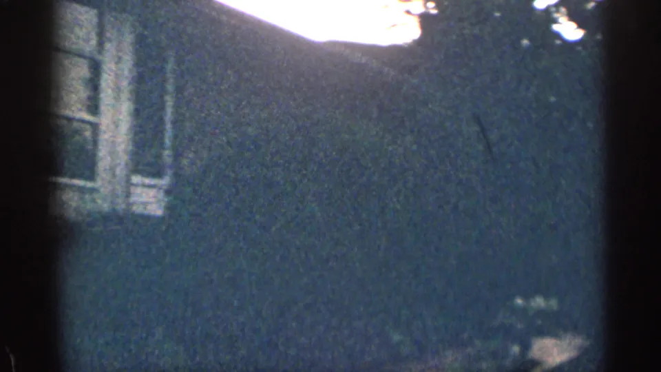 1963 Texas 8mm frame with a darker view of the brick building, partial windows, shrubbery, and an overexposed patch near the top edge.