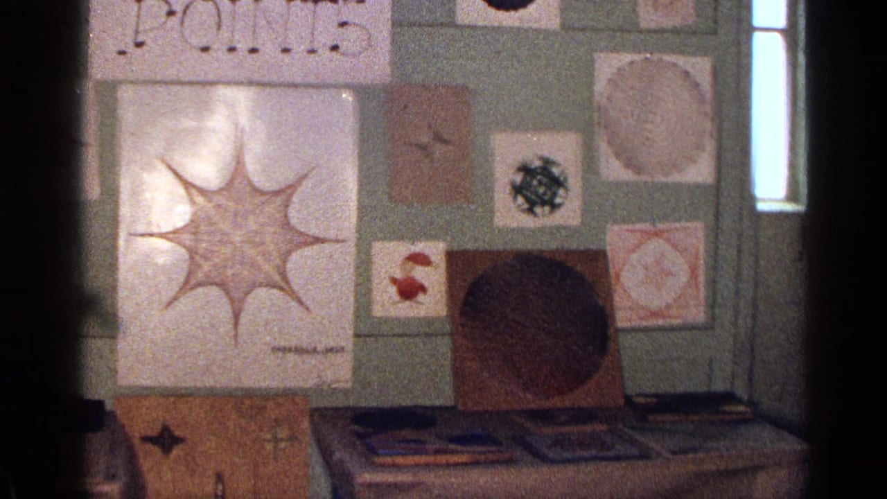 Geometric drawings and abstract art pieces displayed on a green wall above a table.