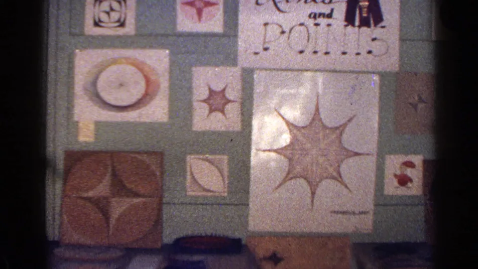 1963 Texas home-movie frame showing a close view of handmade geometric and abstract art on an interior wall.